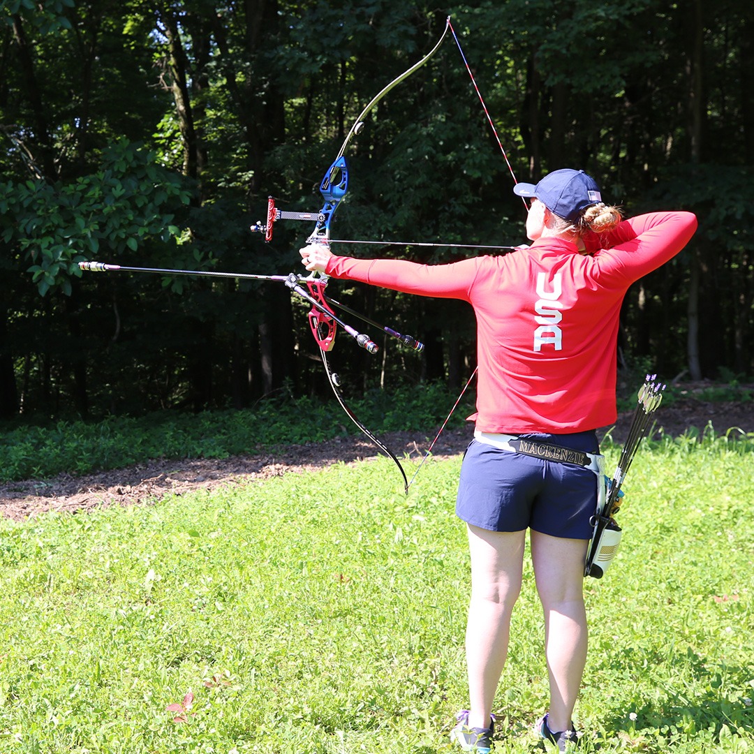 A woman shooting a compound bow on grass