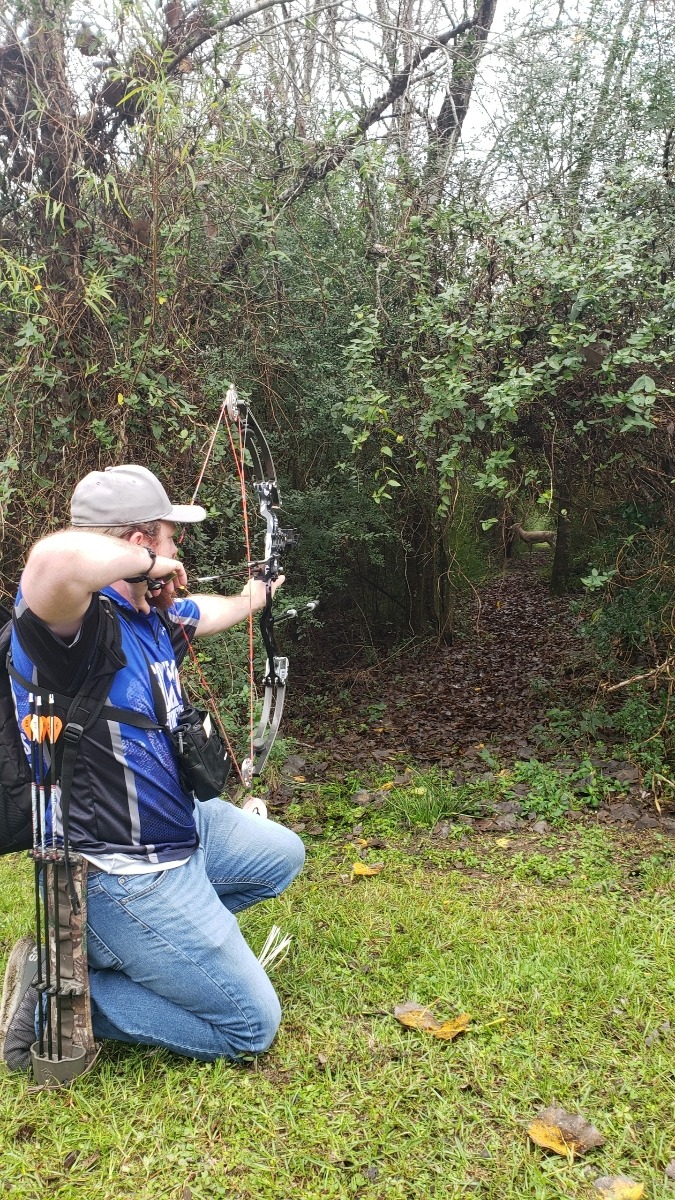  An archer kneels in the forest to prepare a shot with his compound bow. In archery, price tag concerns are a growing problem