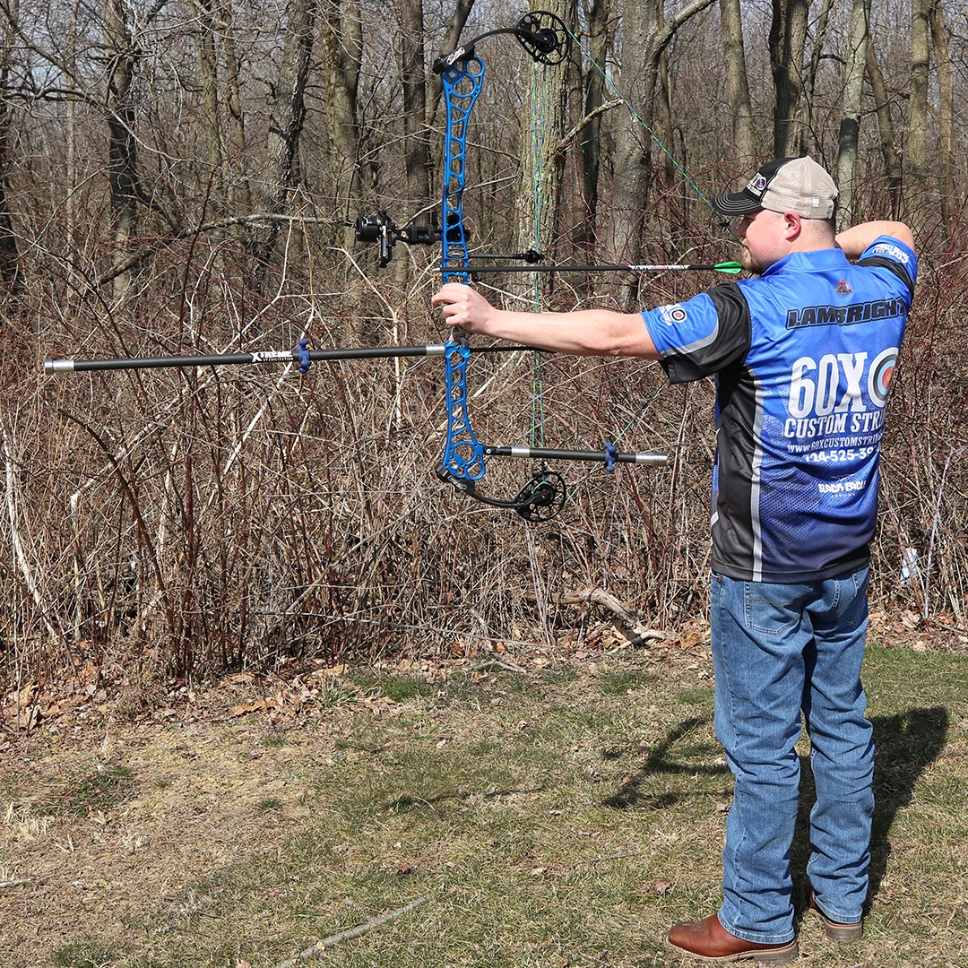 A man outside shooting a compound bow