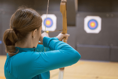 rear view of woman aiming arrow at indoor range