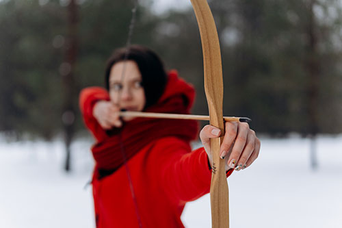 selective focus of woman in red jacket drawing bow