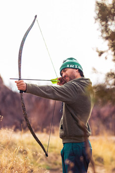 side view of man holding drawn bow with knocked arrow